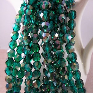May include: Strands of faceted, emerald green beads. The beads have a multi-faceted cut, reflecting light with iridescent flashes of color. The beads are strung together, creating a flowing, textured appearance. The beads are displayed against a white background.