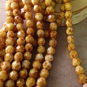 May include: Strands of faceted, round beads in shades of cream and brown. The beads have a speckled pattern and a glossy finish. The beads are strung together, creating a necklace or bracelet.