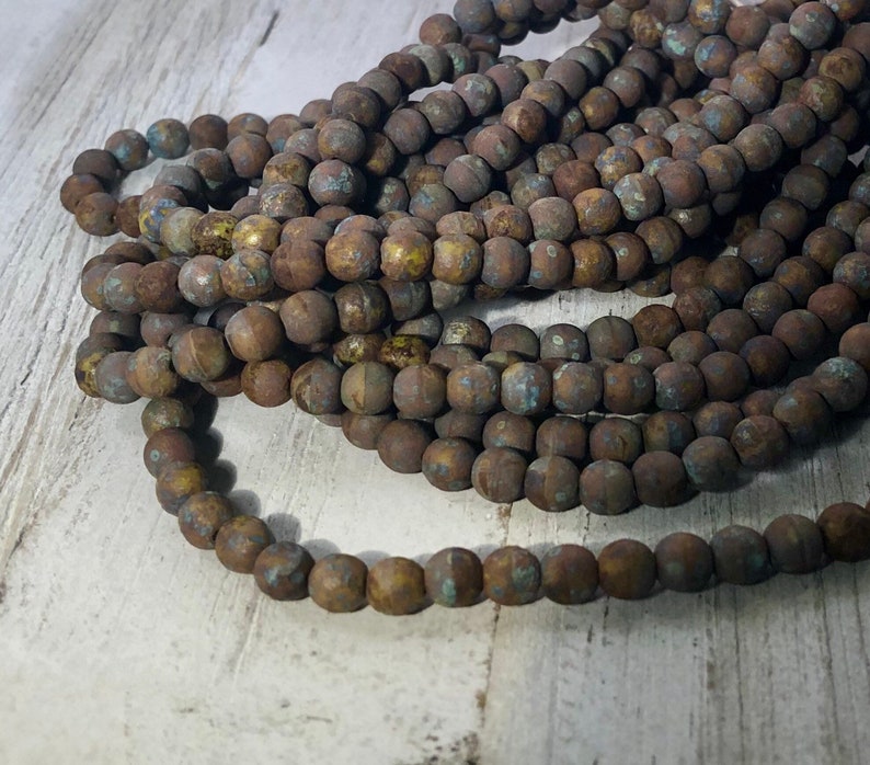 May include: Strands of round, rustic-looking beads in varying shades of brown with hints of blue and yellow. The beads have a textured, weathered appearance, suggesting an aged or antique aesthetic. The beads are likely used for jewelry making or crafting.