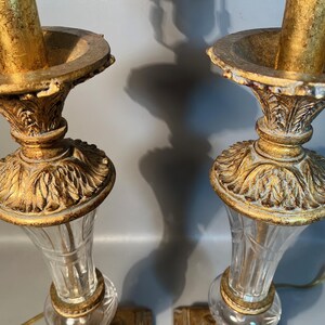 May include: Two ornate gold-coloured candle holders with clear glass bases. The candle holders have a detailed, vintage design with a fluted glass body and a decorative, gold-coloured top.