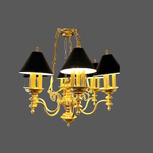 May include: A gold-toned metal chandelier featuring five curved arms, each supporting a light fixture with a black conical shade. The central structure includes a decorative vertical column and a chain suspension system, emitting a warm light.