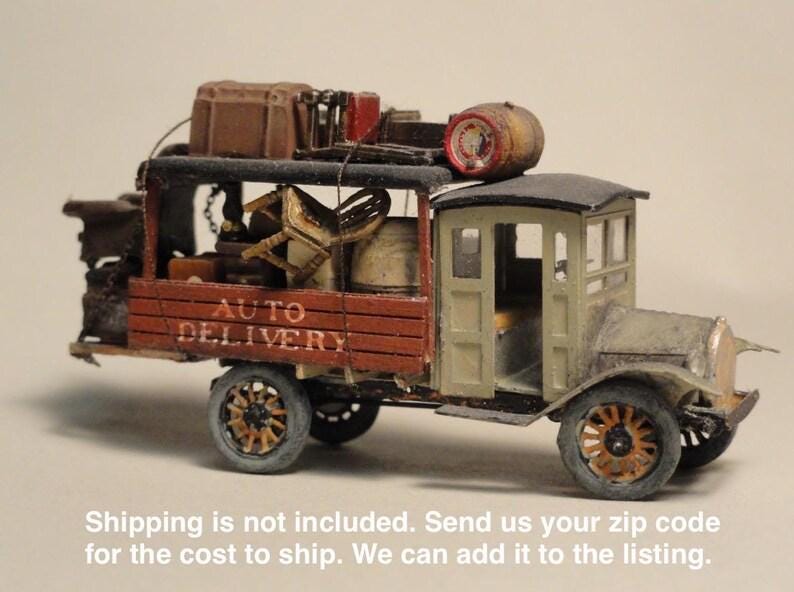 May include: A miniature antique delivery truck with the words "AUTO DELIVERY" on the side. The truck is painted in shades of brown, green, and grey, with a detailed interior and cargo on top. The wheels are brown and the truck has a vintage aesthetic.