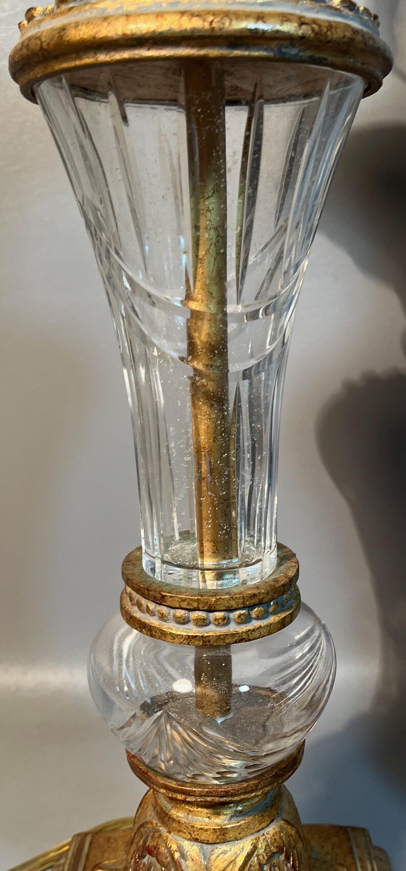 May include: Close-up of a vintage lamp with a clear, etched glass shade and a gold-coloured metal base. The lamp features a decorative, ornate design and a central brass rod.