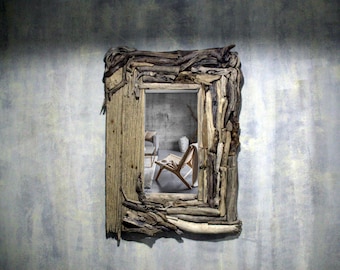 May include: A rustic mirror with a frame made of driftwood. The mirror reflects a room with a chair and a vase.