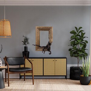 May include: A stylish living room with a black leather chair, a side table, and a woven cabinet. A gold-framed mirror and a woven pendant light adorn the grey wall. Plants in black pots and a woven rug complete the decor.