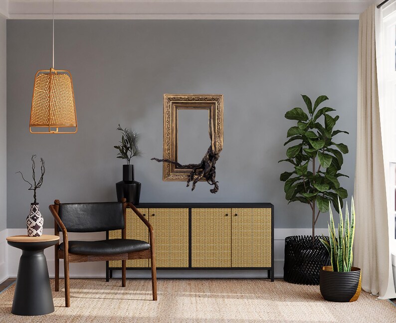 May include: A stylish living room with a black leather chair, a side table, and a woven cabinet. A gold-framed mirror and a woven pendant light adorn the grey wall. Plants in black pots and a woven rug complete the decor.