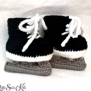 May include: A pair of crocheted baby ice skate booties in black, white, and gray. The booties have a white crocheted trim and a gray crocheted sole.