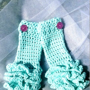 May include: A pair of crocheted baby bloomers with ruffles in a light turquoise color. The bloomers have two pink buttons on the front.