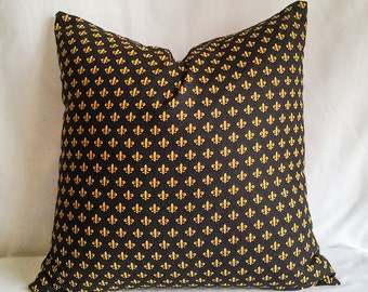 May include: Black and gold decorative throw pillow with a repeating pattern of fleur-de-lis.