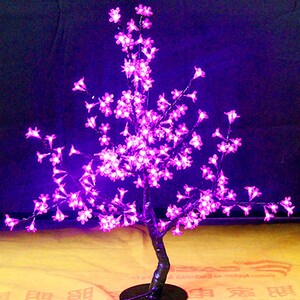 May include: A pink LED cherry blossom tree with a black base and a USB cord. The tree is lit up and the lights are on.