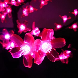 May include: Pink LED lights shaped like cherry blossoms, strung on a wire, against a dark background.