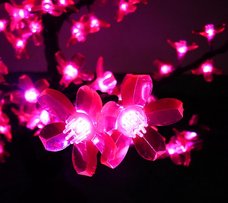 May include: Pink LED lights shaped like cherry blossoms, strung on a wire, against a dark background.