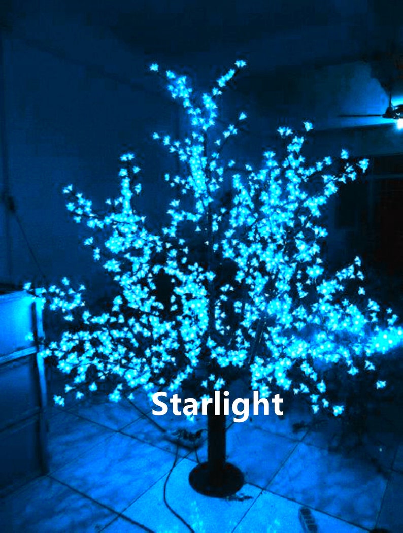 May include: A blue LED light-up tree with a black base. The tree is decorated with small white lights that resemble blossoms. The text "Starlight" is visible on the base of the tree.