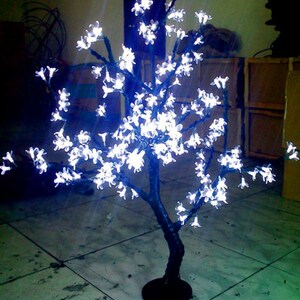 May include: A white LED light-up cherry blossom tree with a black base. The tree is decorated with white lights that resemble cherry blossoms.