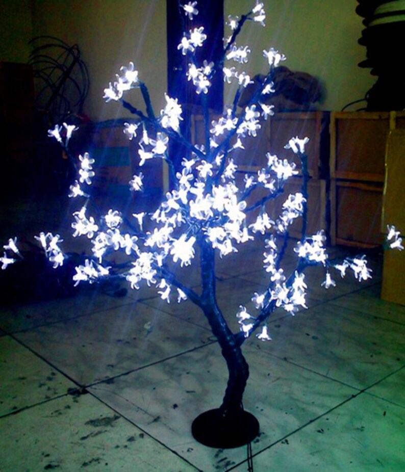 May include: A white LED light-up cherry blossom tree with a black base. The tree is decorated with white lights that resemble cherry blossoms.
