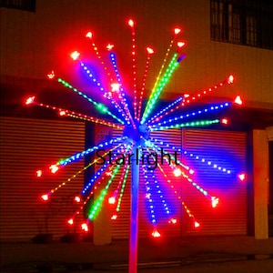Può includere: Un display luminoso a LED a forma di stella. Le luci si irradiano da una sfera blu centrale, con luci rosse, verdi e blu. La parola "Starlight" è visibile sul display. Questa luce decorativa è adatta per uso esterno.