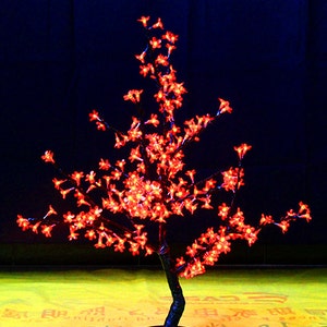 May include: A red LED cherry blossom tree with a black base and a black cord. The tree is lit up and the lights are on.
