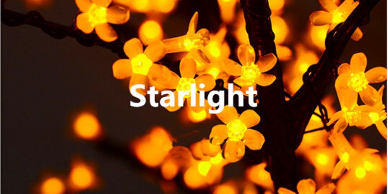 May include: A string of warm white fairy lights shaped like flowers. The lights are strung on a black wire and the text "Starlight" is visible in the center of the image.