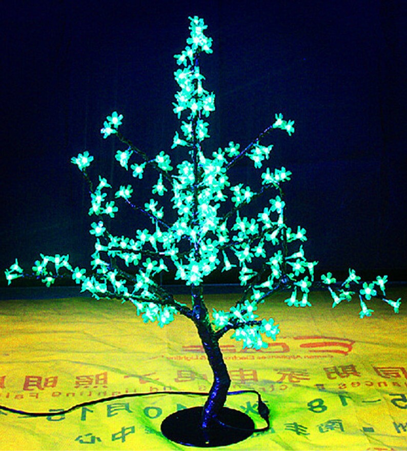May include: A decorative LED light-up tree with a black base and green lights shaped like flowers. The tree is on a yellow surface with Chinese characters.