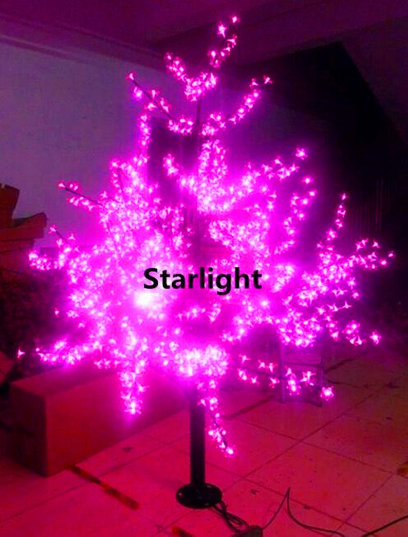 May include: A pink LED light-up tree with a black metal base. The tree is decorated with small pink lights that resemble blossoms. The text "Starlight" is visible on the tree.