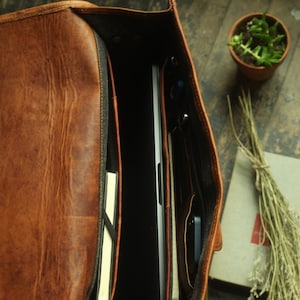 May include: A brown leather messenger bag with a laptop, notebook, and phone inside. The bag has a zippered closure and a flap with a buckle.
