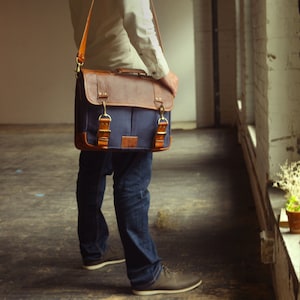 K&ouml;nnte beinhalten: Eine Person in blauen Jeans und einem wei&szlig;en Hemd tr&auml;gt eine braune Leder- und blaue Canvas-Messenger-Tasche mit einem langen Riemen &uuml;ber der Schulter.
