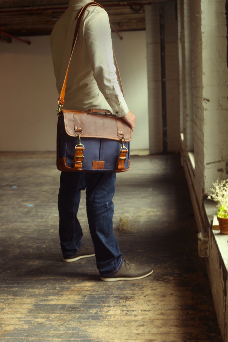 K&ouml;nnte beinhalten: Eine Person in blauen Jeans und einem wei&szlig;en Hemd tr&auml;gt eine braune Leder- und blaue Canvas-Messenger-Tasche mit einem langen Riemen &uuml;ber der Schulter.