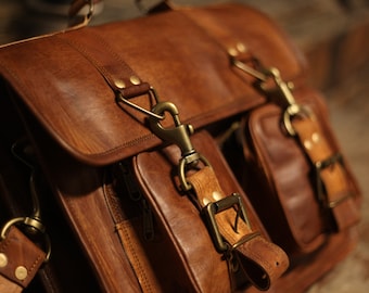 May include: A brown leather satchel bag with brass hardware and multiple pockets. The bag has a strap and a buckle closure.