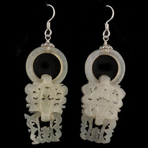 May include: A pair of white jade earrings with intricate carvings. The earrings feature a circular design with a dangling pendant. The pendants are carved with floral and geometric patterns.