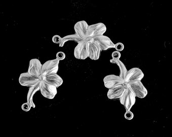 Könnte beinhalten: Drei silberne Blumenanhänger mit einer Schlaufe an jeder Seite. Die Blumen haben fünf Blütenblätter und ein zentrales Detail.