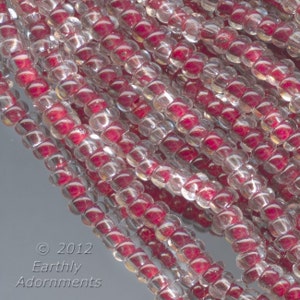 May include: Close-up of a strand of clear glass seed beads with a red iridescent sheen. The beads are small and round, and they are arranged in a random pattern.