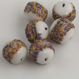 May include: Six white glass beads with a speckled pattern of blue, orange, and yellow. The beads have a hole through the centre.