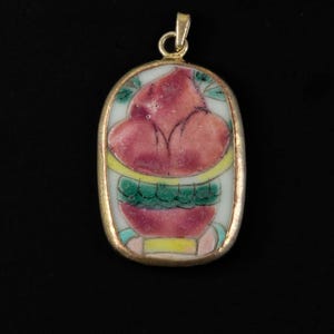 May include: A gold-toned pendant with a white porcelain oval inset. The porcelain is painted with a pink flower in a green and yellow pot.