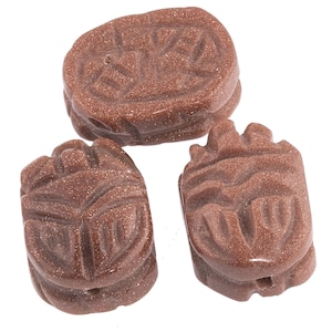 May include: Three brown sandstone scarab beetle beads with intricate carvings. The beads are oval shaped and have a hole drilled through the centre for stringing.