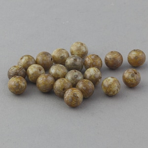May include: A collection of round beads with a mottled, earthy appearance. The beads are primarily tan and brown, with variations in color and pattern. They appear to be made of a natural material, possibly stone or wood, and are scattered on a neutral gray surface.