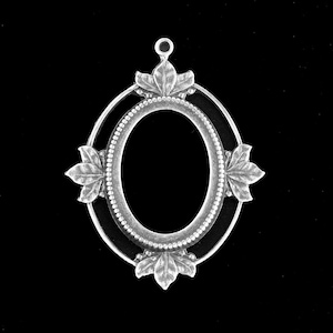 以下が含まれることがあります： 装飾的な縁取りと葉のアクセントが付いた銀製の楕円形のペンダント。ペンダントの中央には、写真やその他の装飾品を入れるための空白があります。