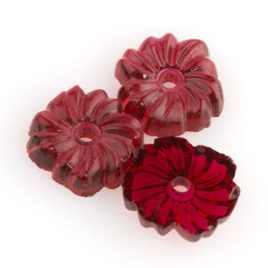 May include: Three red glass flower-shaped beads with a hole in the center. The beads are translucent and have a slightly textured surface.