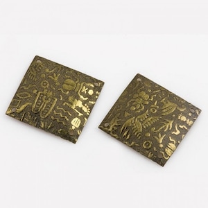 May include: Two gold-colored metal square embellishments with intricate embossed designs. The embellishments have four holes in the corners.