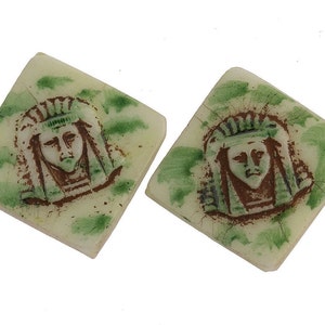 May include: Two square ceramic tiles with a green and white background. Each tile features a brown image of a person's face wearing a crown and a long, flowing garment.