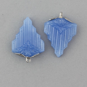 May include: Two light blue art deco style pendants. Each pendant has a silver-colored metal cap with a loop. The pendants have a geometric design with vertical lines and a floral motif at the bottom.