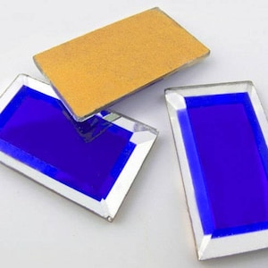 Puede incluir: Tres azulejos de vidrio rectangulares con un borde plateado y un centro azul. Los azulejos están sobre una superficie blanca.