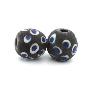May include: Two black glass beads with white and blue eye designs. The beads are round and have a glossy finish.