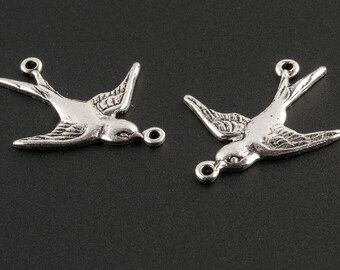 Könnte beinhalten: Zwei silberfarbene Vogel-Anhänger aus Metall mit einer Öse zum Anbringen an einer Halskette oder einem Armband. Die Vögel befinden sich in Flugposition mit ausgebreiteten Flügeln.