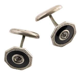 May include: A pair of silver cufflinks with black enamel and a clear rhinestone in the center of each cufflink.