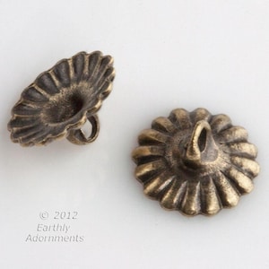 Puede incluir: Dos botones de metal de color dorado antiguo con un borde festoneado y un centro elevado. Los botones tienen un lazo en la parte superior para sujetarlos a una prenda.