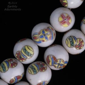 May include: Close-up of white ceramic beads with colourful floral and geometric designs. The beads feature yellow, red, blue, and green accents. The image includes the text "© 2014 Earthly Adornments".