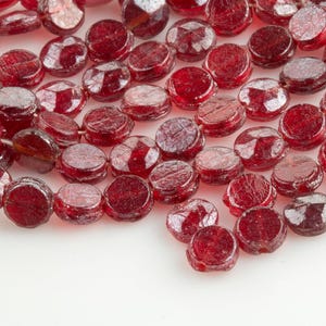 May include: A strand of red glass beads with a faceted, slightly irregular, round shape. The beads have a sparkly, iridescent finish.