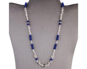 Op de afbeelding: Een lange ketting gemaakt van heldere en donkerblauwe glazen kralen. De ketting is om de nek van een mannequin.