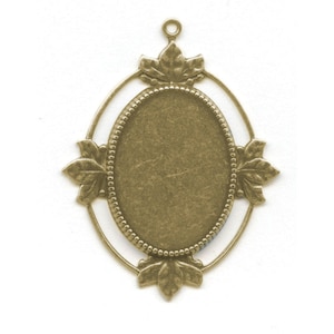 May include: A gold-toned metal pendant with an oval-shaped frame and a decorative leaf design. The frame is designed to hold a cameo or other decorative element.