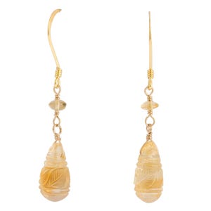 May include: A pair of gold-coloured drop earrings. Each earring features a carved, teardrop-shaped, light yellow gemstone pendant with leaf details. The earrings have a gold-coloured hook and are accented with small, round, light yellow beads.